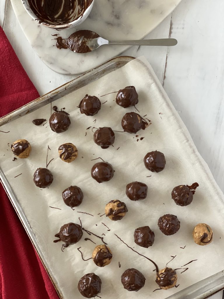 Chocolate covered peanut butter granola bites on a tray with chocolate covered spoon and bowl