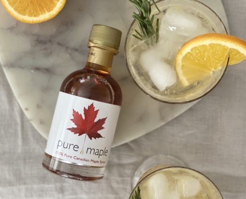 2 glasses of Maple Citrus Spritz with Pure Maple Syrup bottle to the side and half an orange at the top