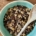 Christmas pudding in a large mixing bowl with a wooden spoon on the side and a bottle of maple syrup at the top