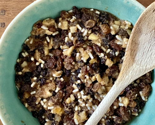 Christmas pudding in a large mixing bowl with a wooden spoon on the side and a bottle of maple syrup at the top