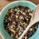 Christmas pudding in a large mixing bowl with a wooden spoon on the side and a bottle of maple syrup at the top