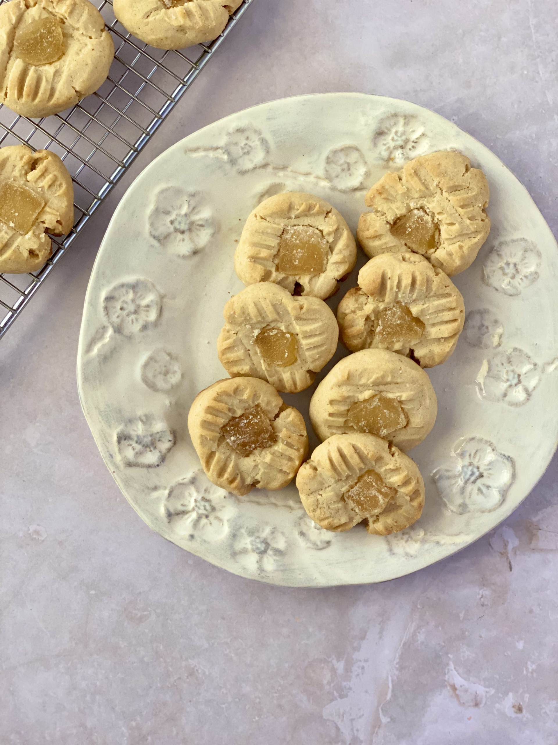 Maple ginger biscuits on a plate with some biscuits on a wire rack at the top left hand corner